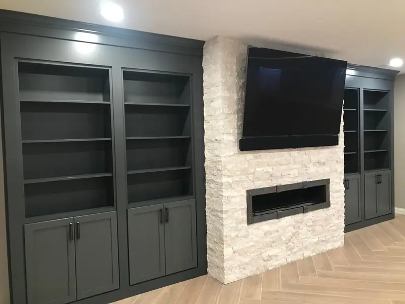 Finished basement media wall with dark built-in shelving and a linear fireplace