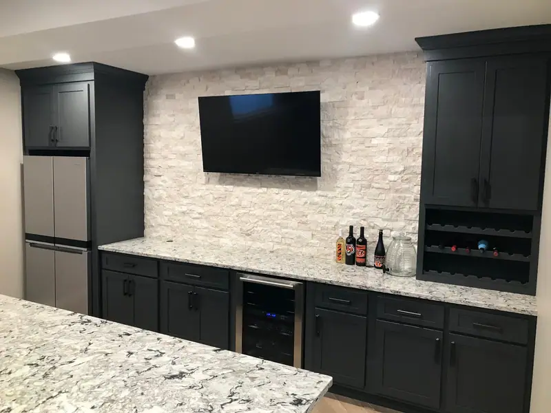 Basement wet bar with dark cabinetry and stone wall