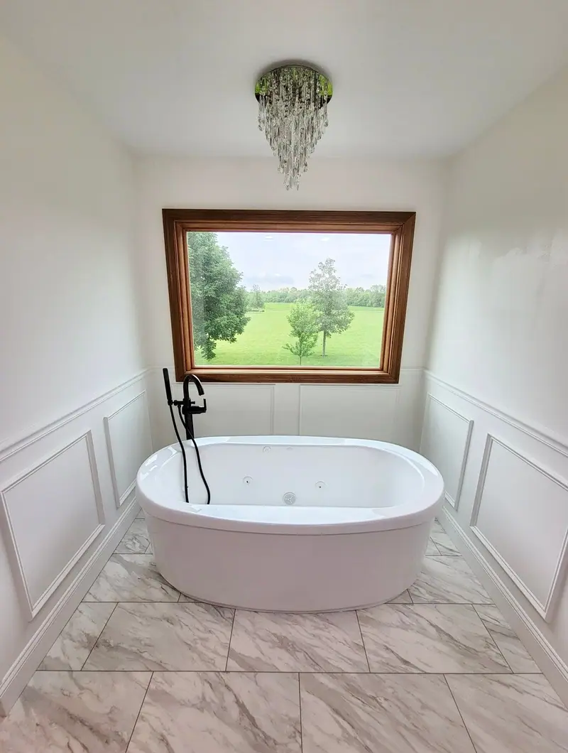 Soaking tub beneath a picture window with wainscoting
