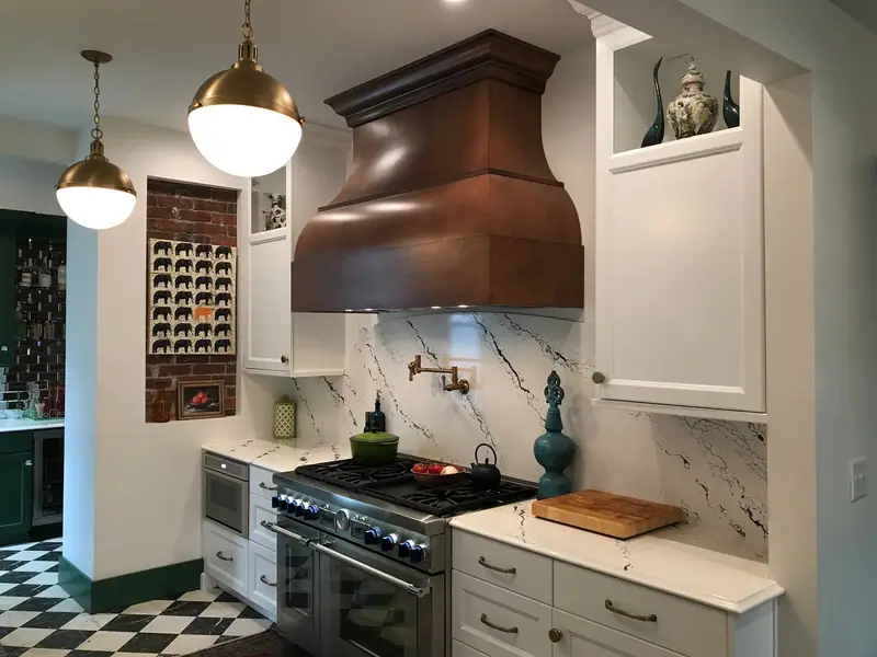 Kitchen with copper range hood, marble backsplash and brass pendants
