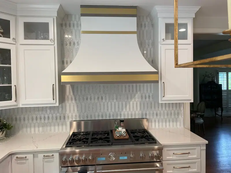 White range hood with brass trim over a gas range and patterned tile
