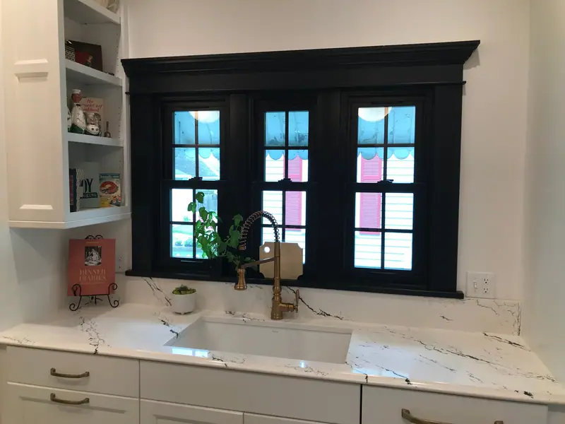 Kitchen sink beneath black-framed windows with quartz counters