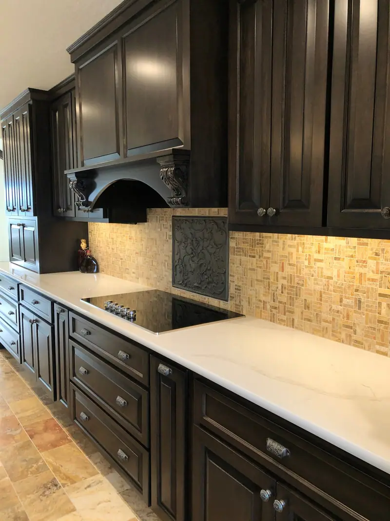 Dark cabinetry with mosaic tile backsplash and cooktop