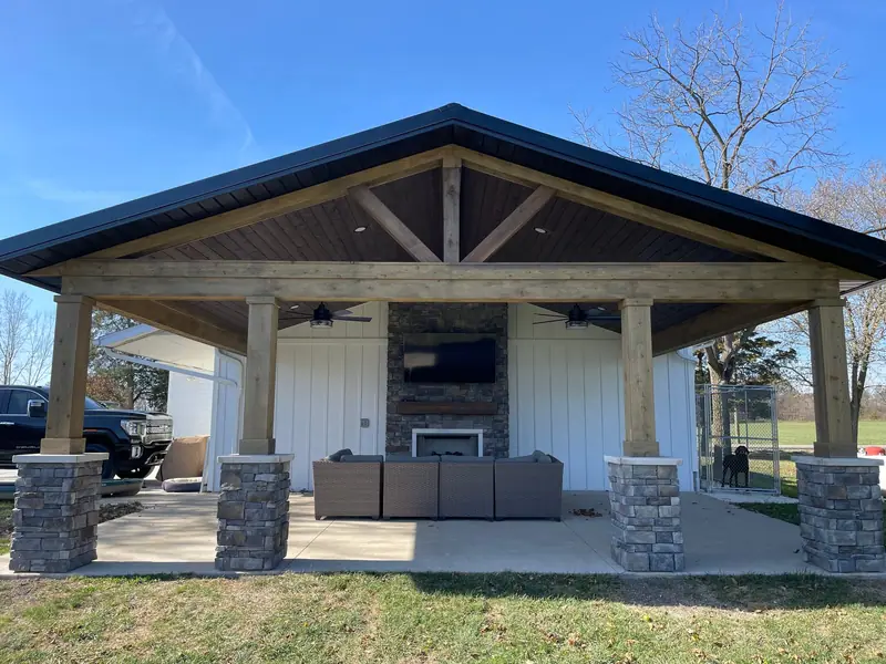 Timber frame outdoor pavilion with stone column bases and an outdoor fireplace