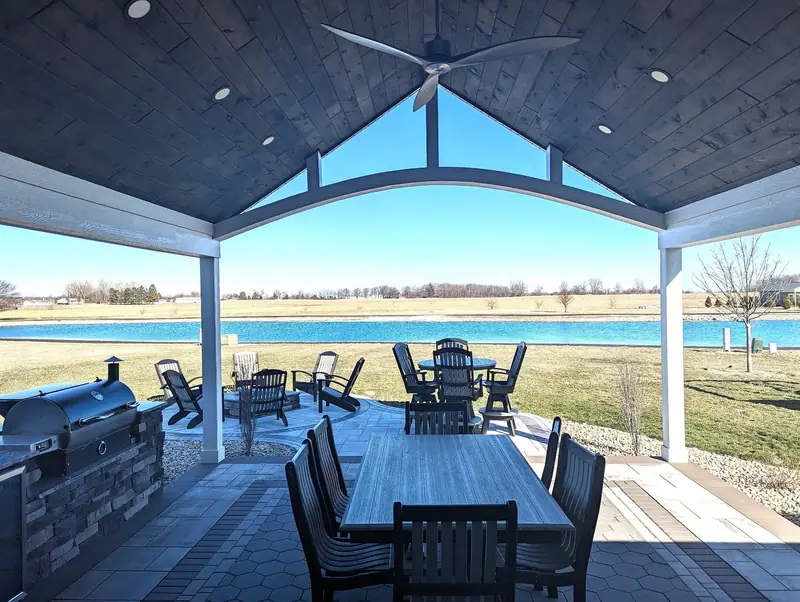 Covered patio with outdoor kitchen and dining area overlooking a pond